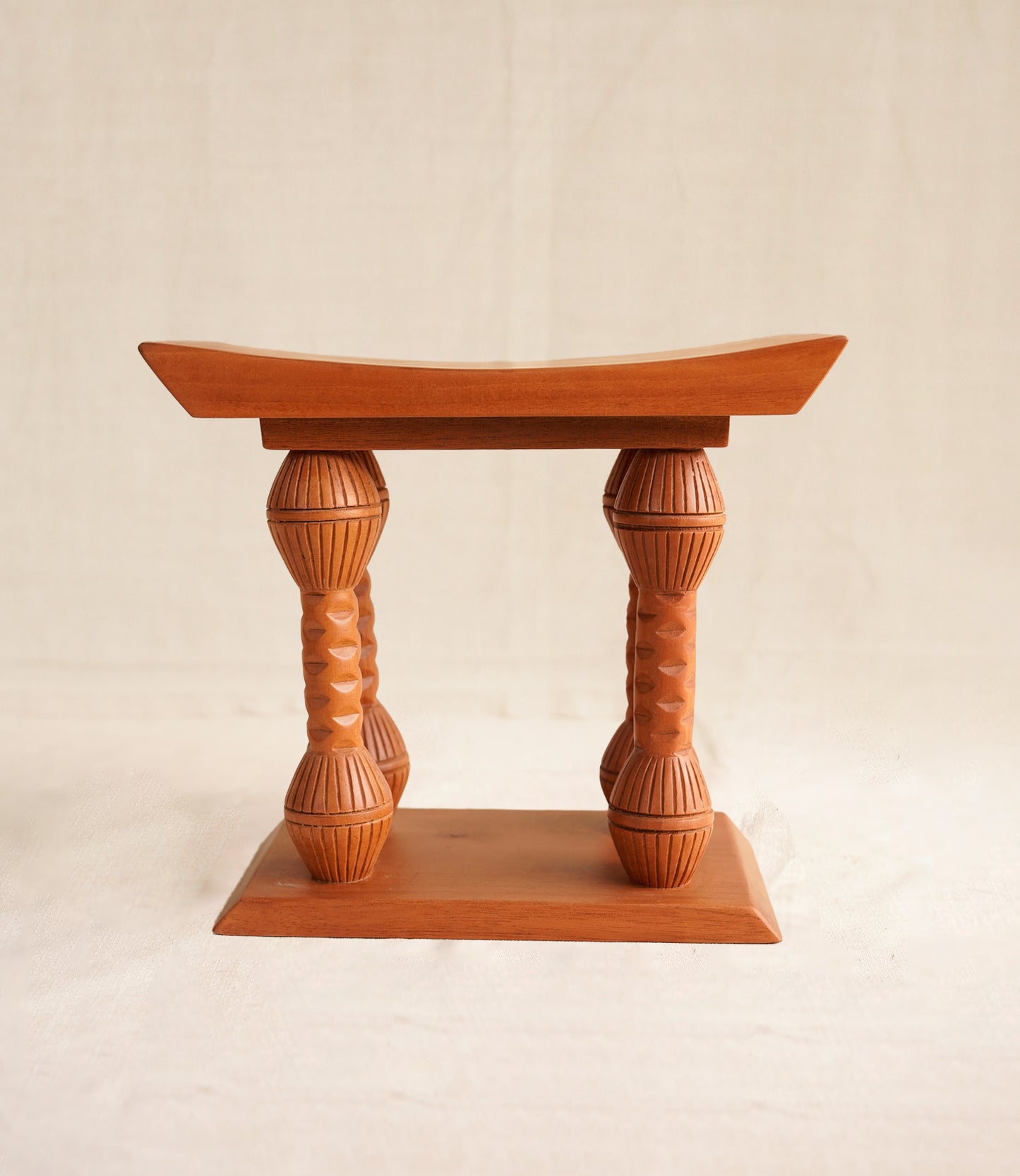Wooden stool with a curved top and textured cylindrical legs on a beige background