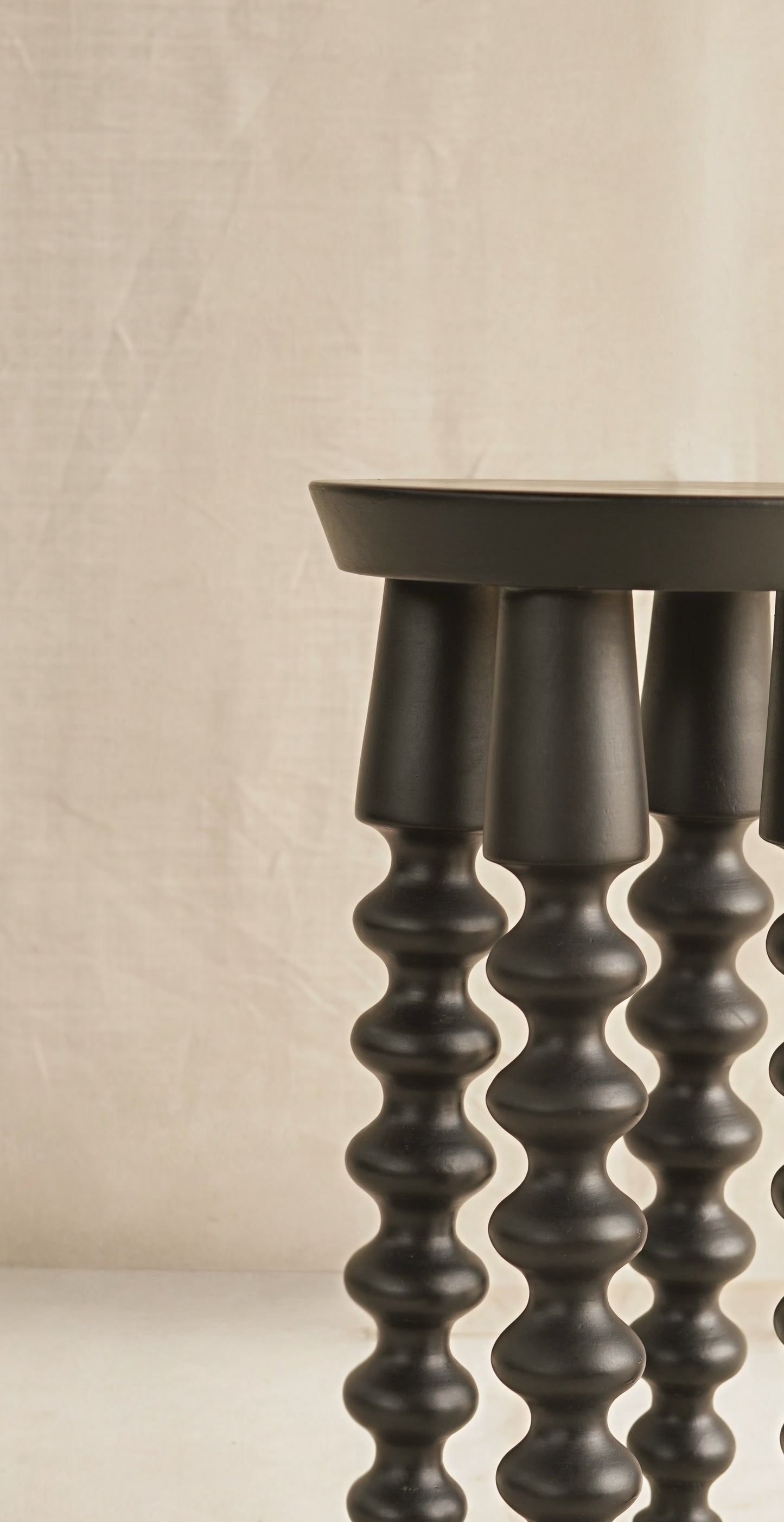 Dark wooden stool with spiral design legs on a beige background