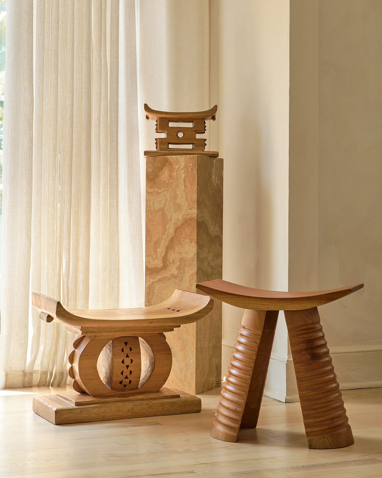 Three wooden stools of different designs on a light wood floor with a neutral wall background.