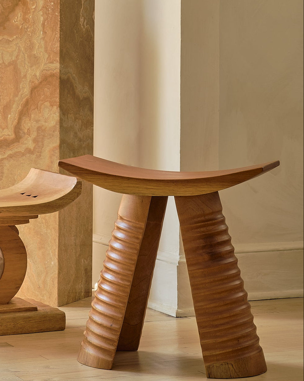 Three wooden stools of different designs on a light wood floor with a neutral wall background.