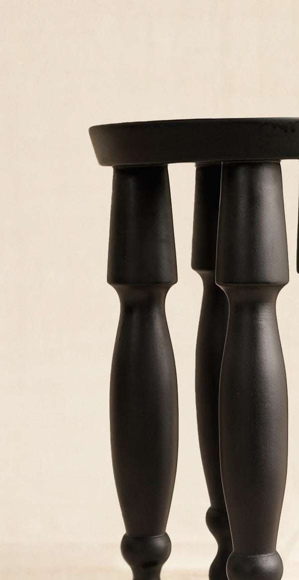 Close-up of a black stool with wooden legs on a beige background
