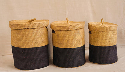 Three handwoven Bolga storage baskets in varying sizes with lids, featuring a natural and black color pattern, made from elephant grass