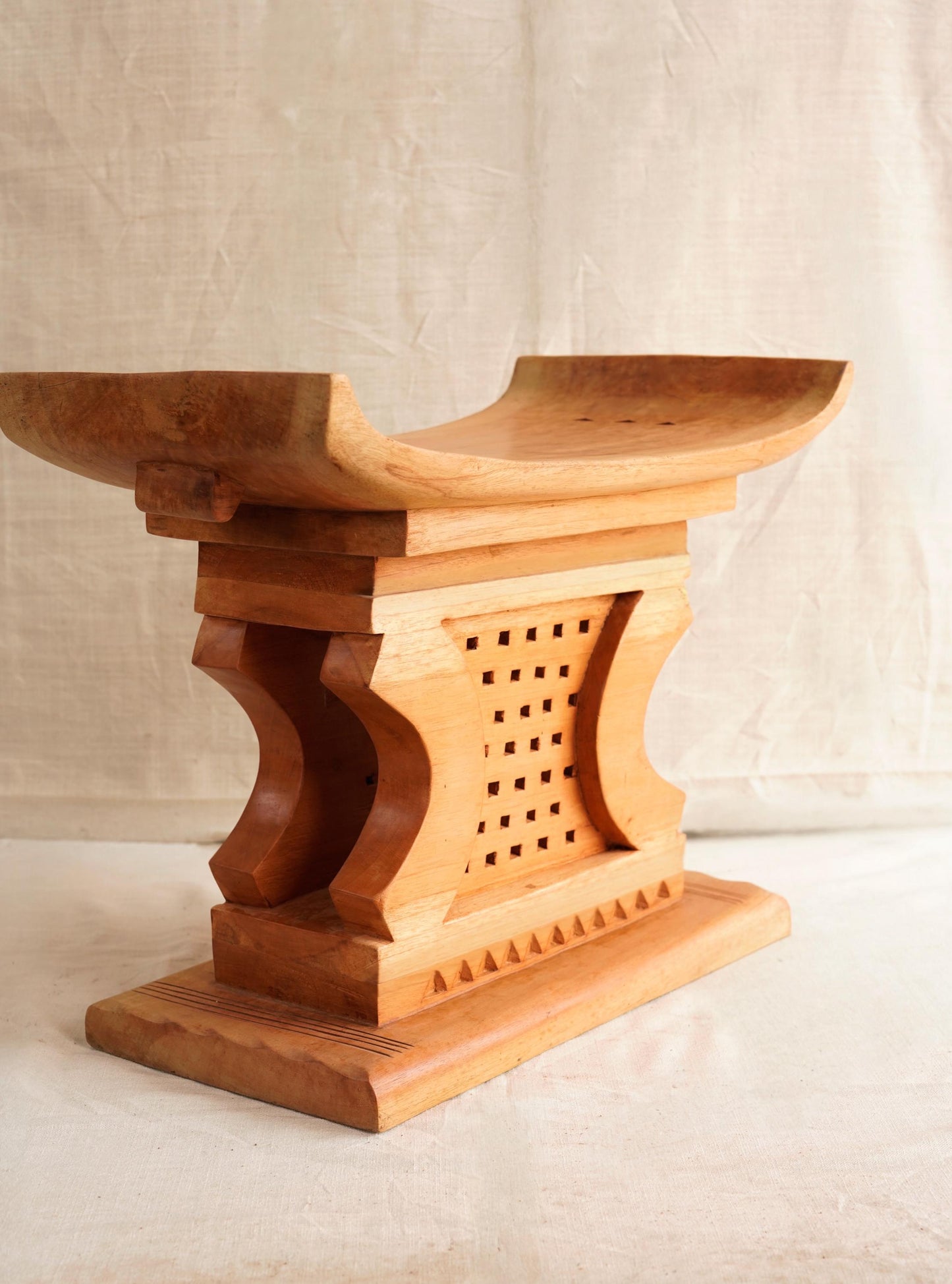A hand-carved wooden Ashanti stool with a curved seat and arched base, featuring traditional tribal motifs.