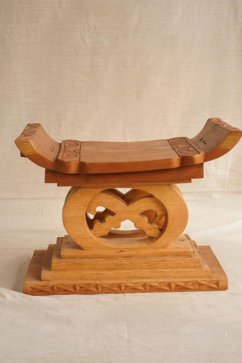 Hand-carved wooden Ashanti stool with a curved seat and arched base, featuring Akan Adinkra symbol 'Akofena'.