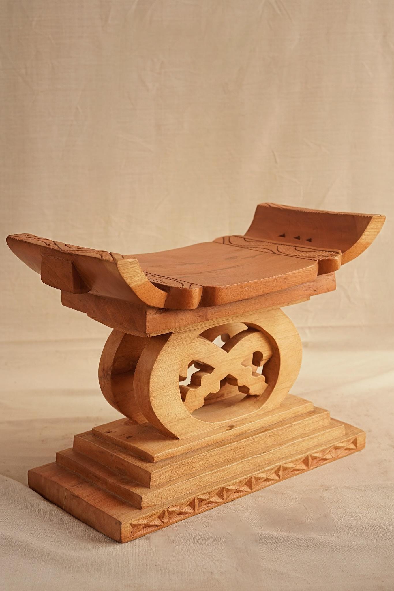 A hand-carved wooden Ashanti stool with a curved seat and arched base, featuring detailed motifs.