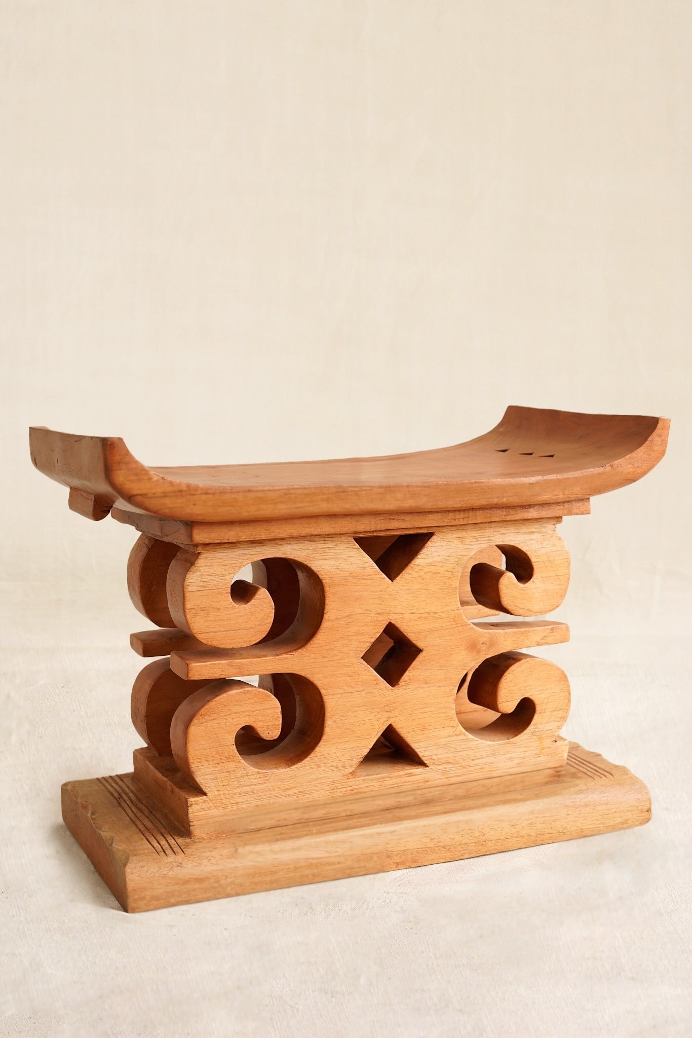Wooden decorative stool with intricate carvings on a beige background