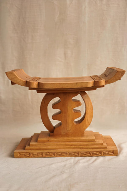 A hand-carved wooden Ashanti stool with a curved seat and arched base, featuring detailed motifs.