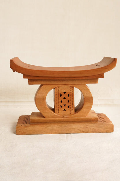 Wooden stool with curved top and decorative base on a beige background