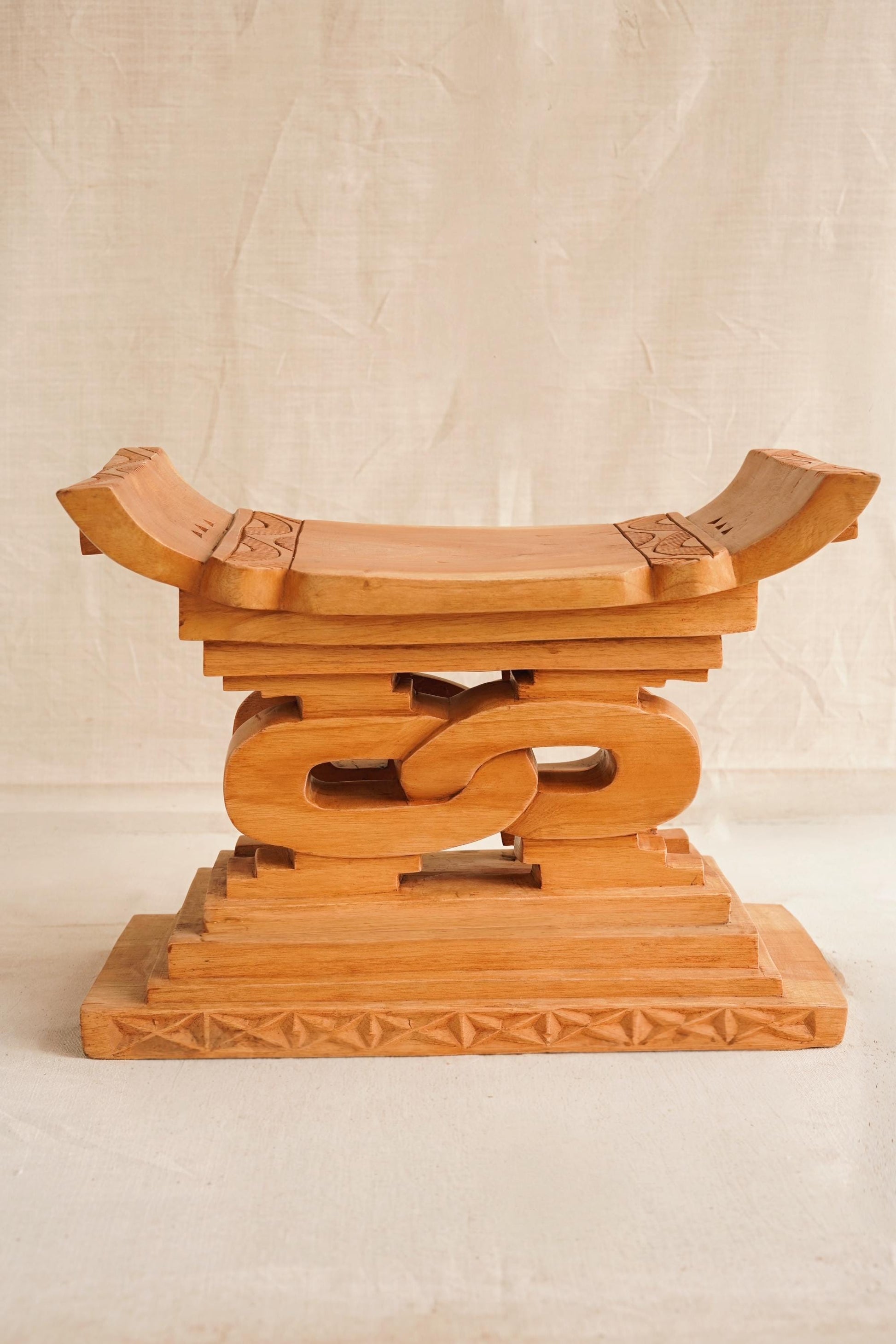 A hand-carved wooden Ashanti stool with a curved seat and arched base, featuring detailed motifs.