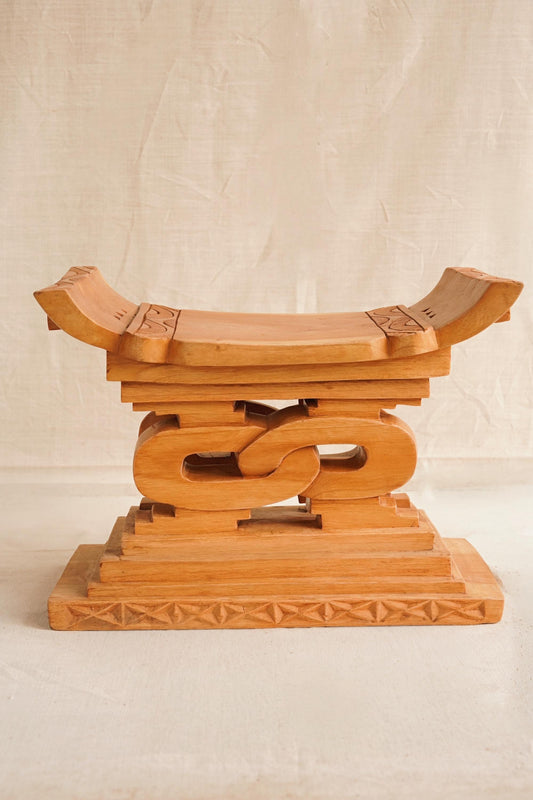 A hand-carved wooden Ashanti stool with a curved seat and arched base, featuring detailed motifs.