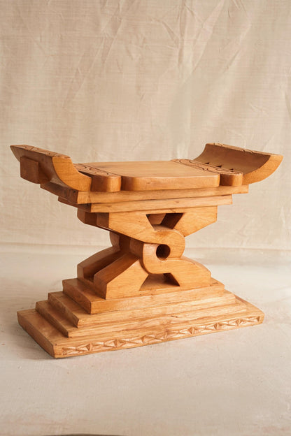 A hand-carved wooden Ashanti stool with a curved seat and arched base, featuring detailed motifs.