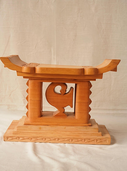 A hand-carved wooden Ashanti stool with a curved seat and arched base, featuring the Akan Adinkra symbol 'Sankofa' on the front.