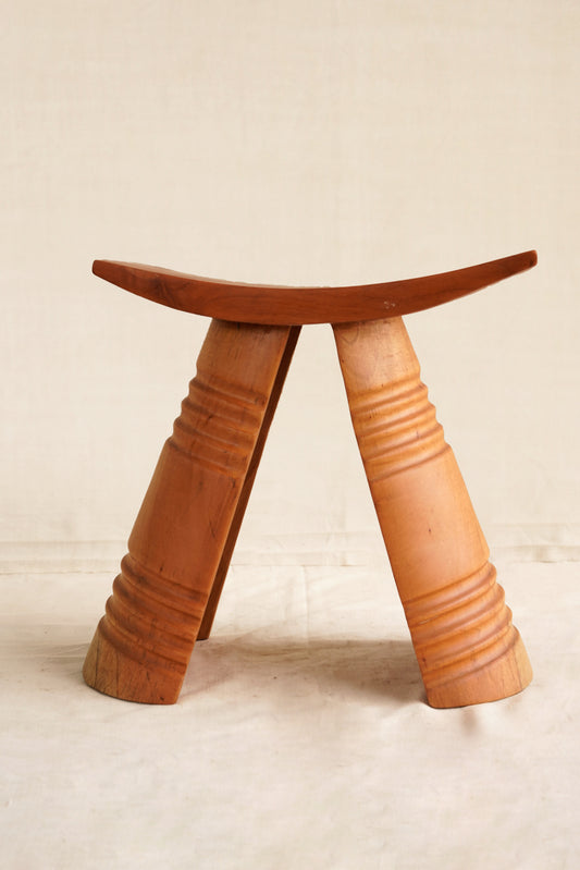 Wooden stool with a curved top and textured legs on a beige background