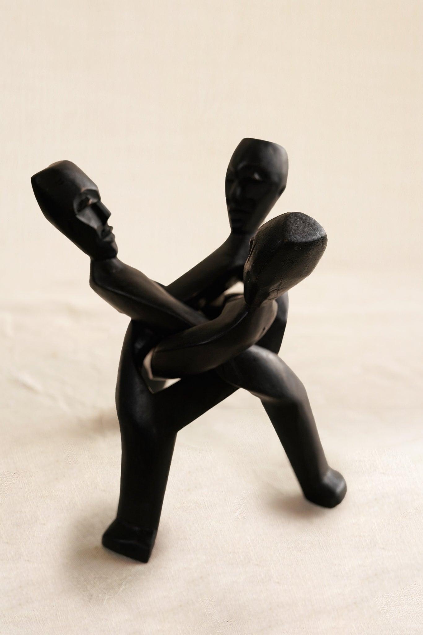 Black figurine of three people embracing on a beige background