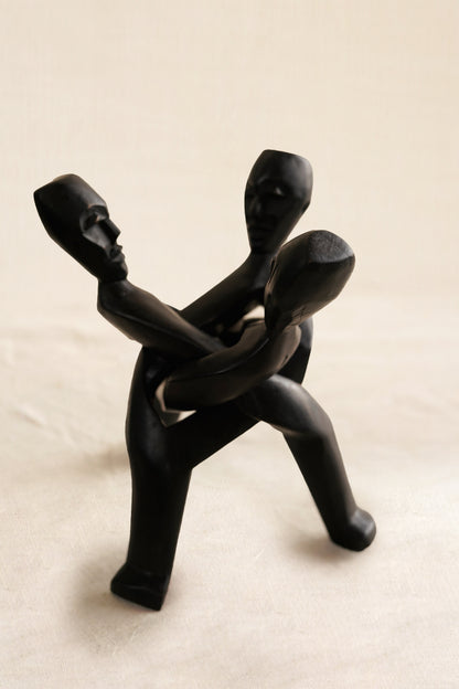 Black figurine of three people embracing on a beige background