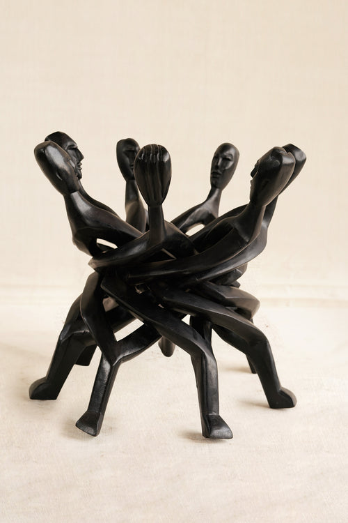 Black abstract sculpture of intertwined figures on a beige background