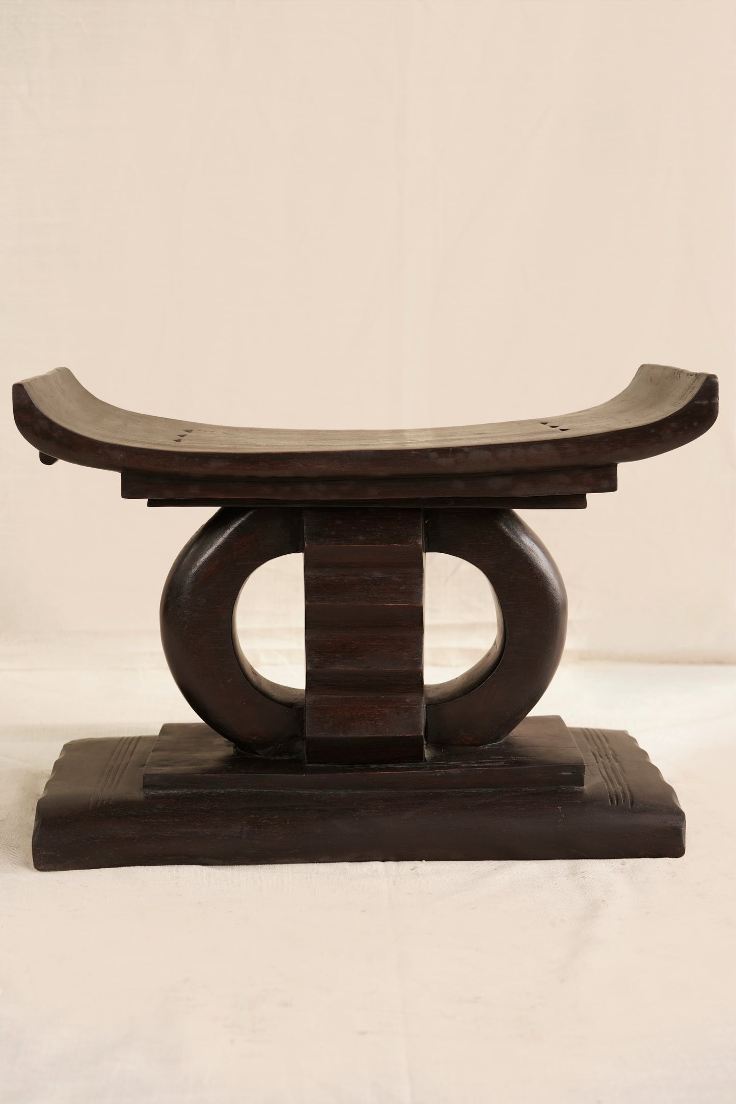 Wooden stool with curved top and circular base on a plain background