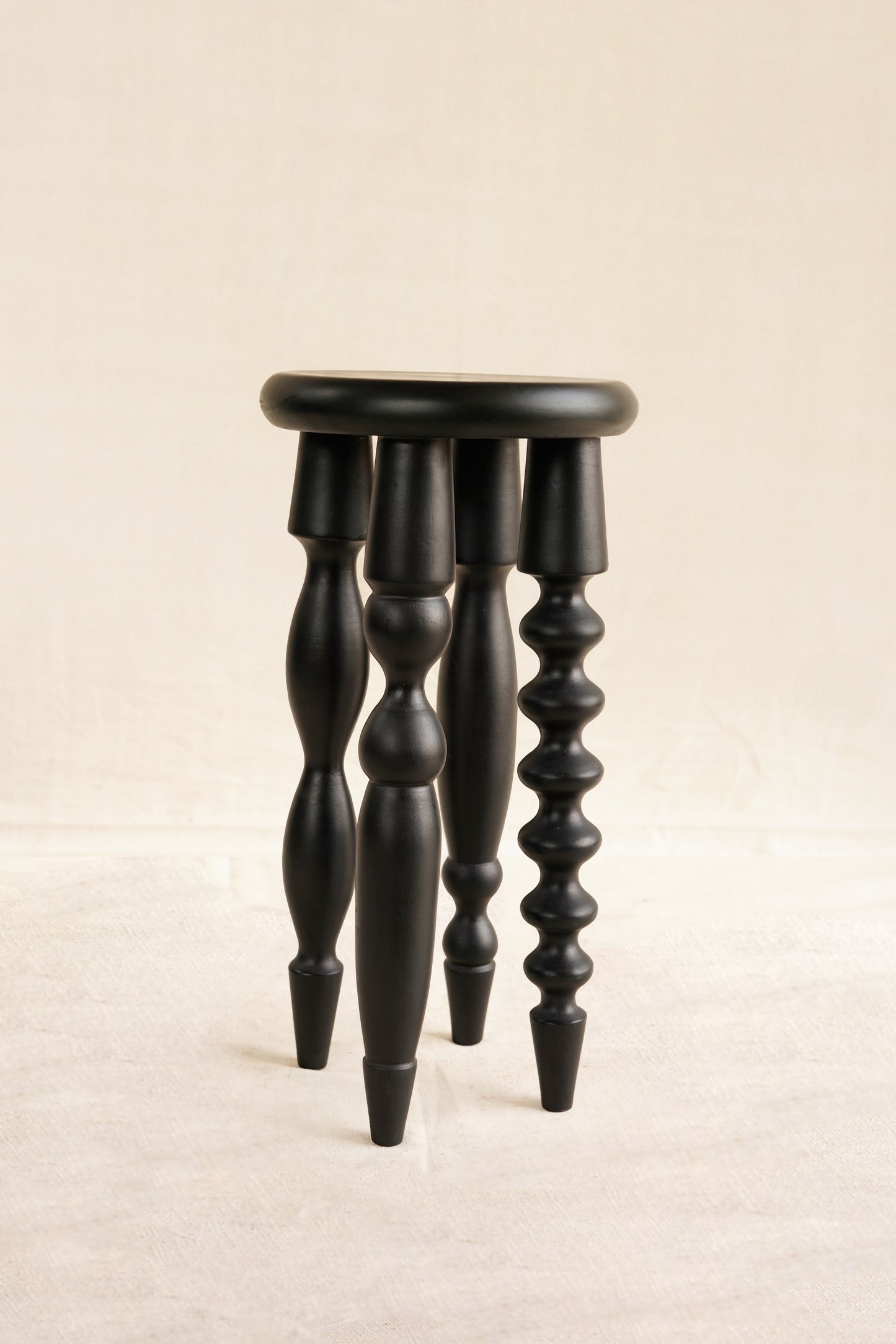 Black wooden stool with spiral legs on a beige background