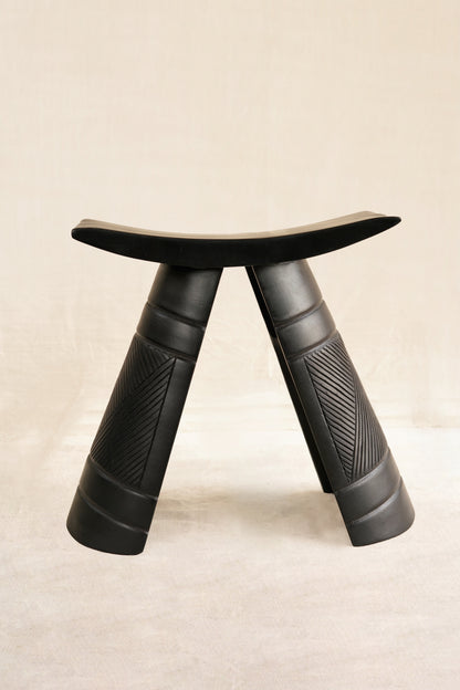 Black wooden stool with textured legs on a beige background