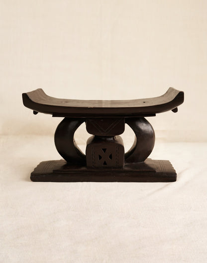 Wooden stool with a curved top and circular base on a beige background