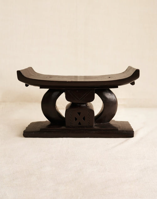 Wooden stool with a curved top and circular base on a beige background