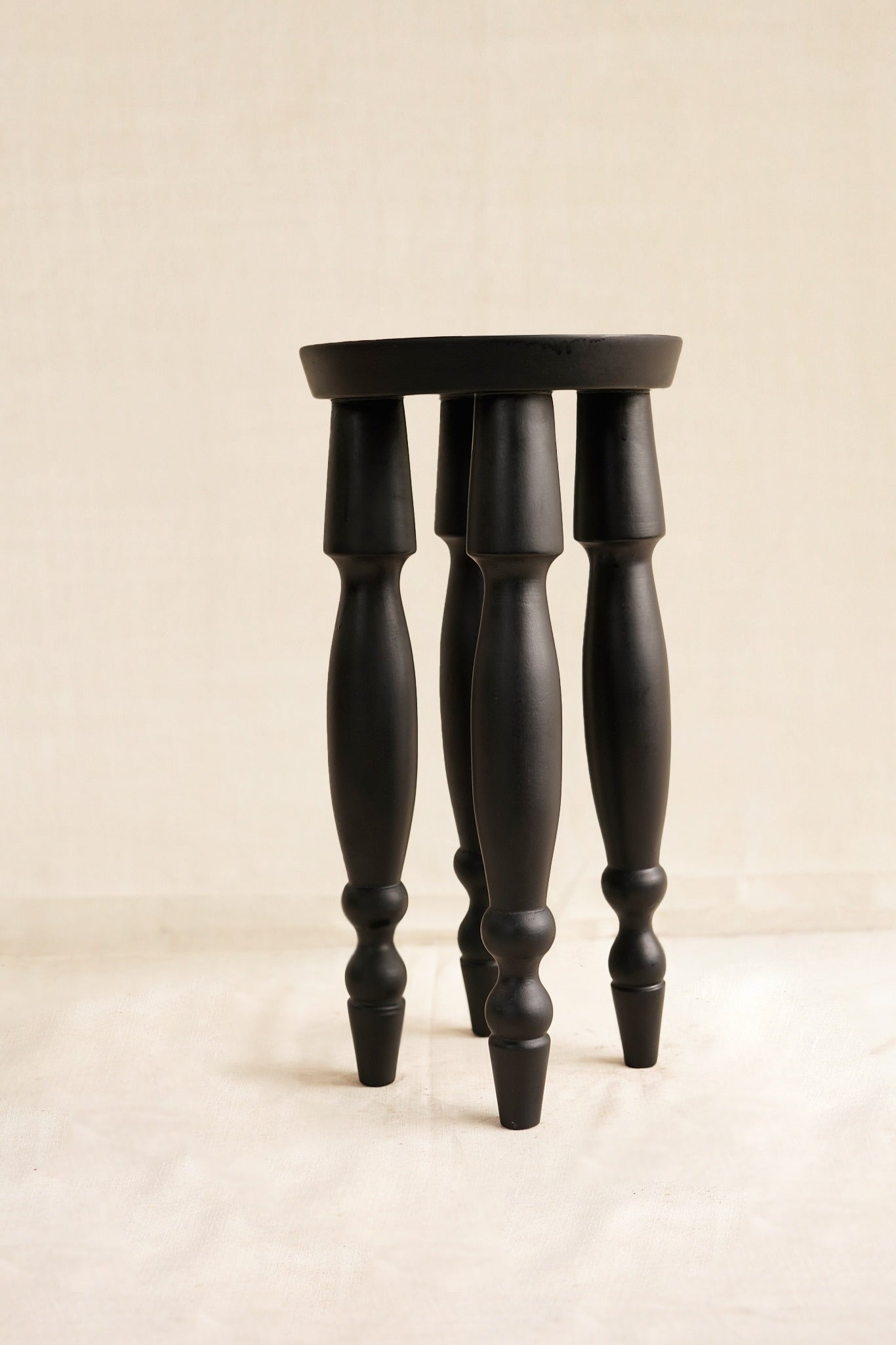 Black wooden stool with turned legs on a beige background