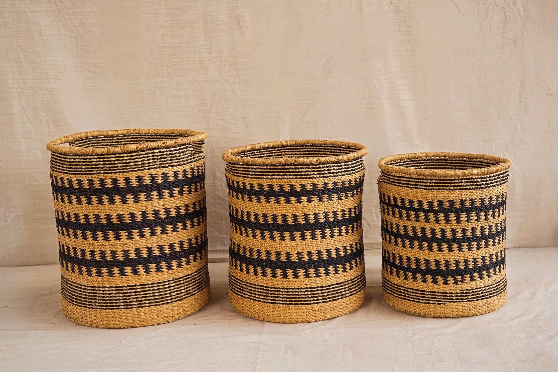 Three handwoven Bolga storage baskets in different sizes, featuring a geometric pattern in beige and black colors with leather-wrapped handles.