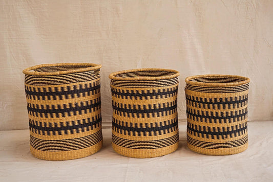 Three handwoven Bolga storage baskets in different sizes, featuring a geometric pattern in beige and black colors with leather-wrapped handles.
