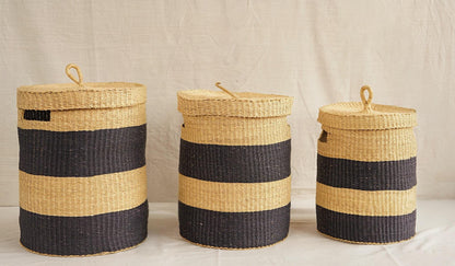 Three handwoven Bolga storage baskets with lids, in varying sizes, featuring natural and black stripes and leather-wrapped handles.