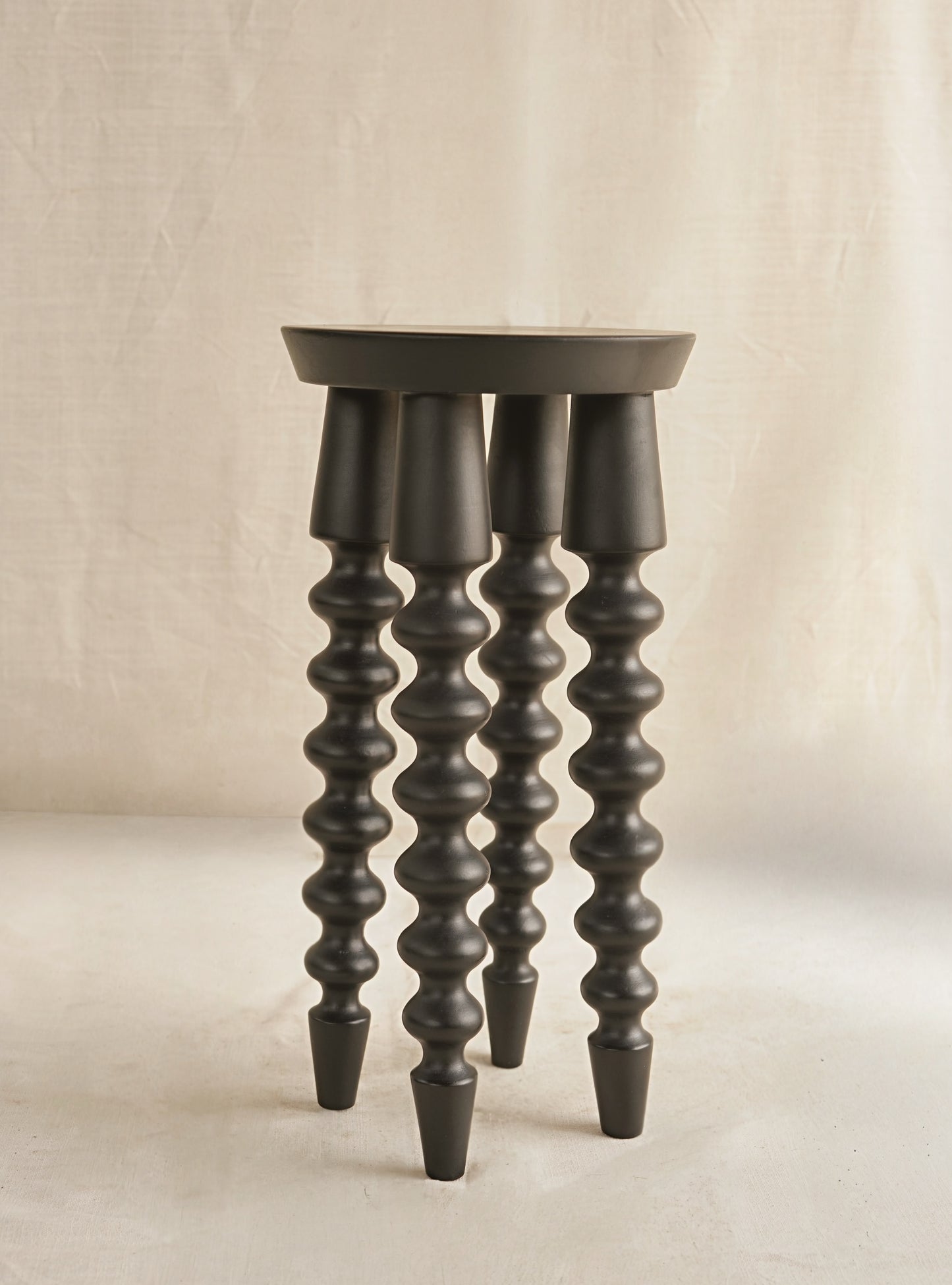 Dark wooden stool with spiral design legs on a beige background