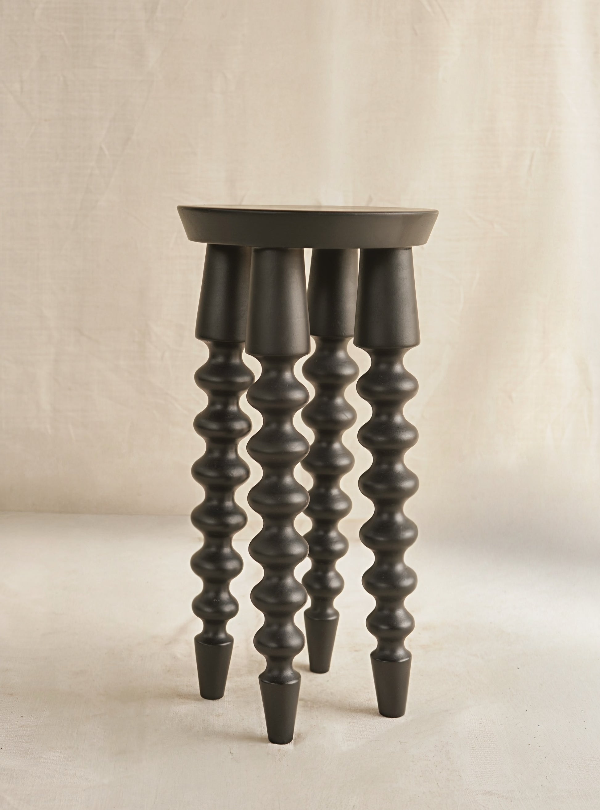 Dark wooden stool with spiral design legs on a beige background