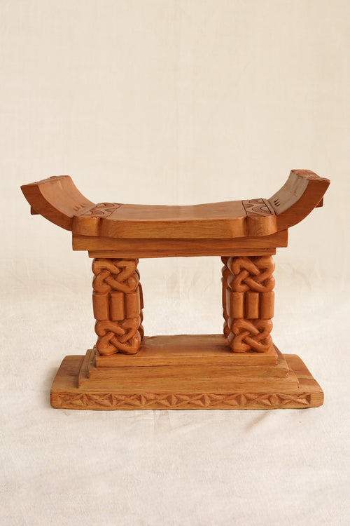 Wooden stool with intricate carvings on a beige background