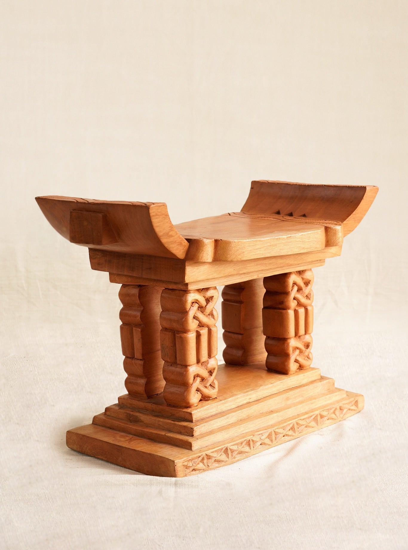 Wooden stool with intricate carvings on a beige background