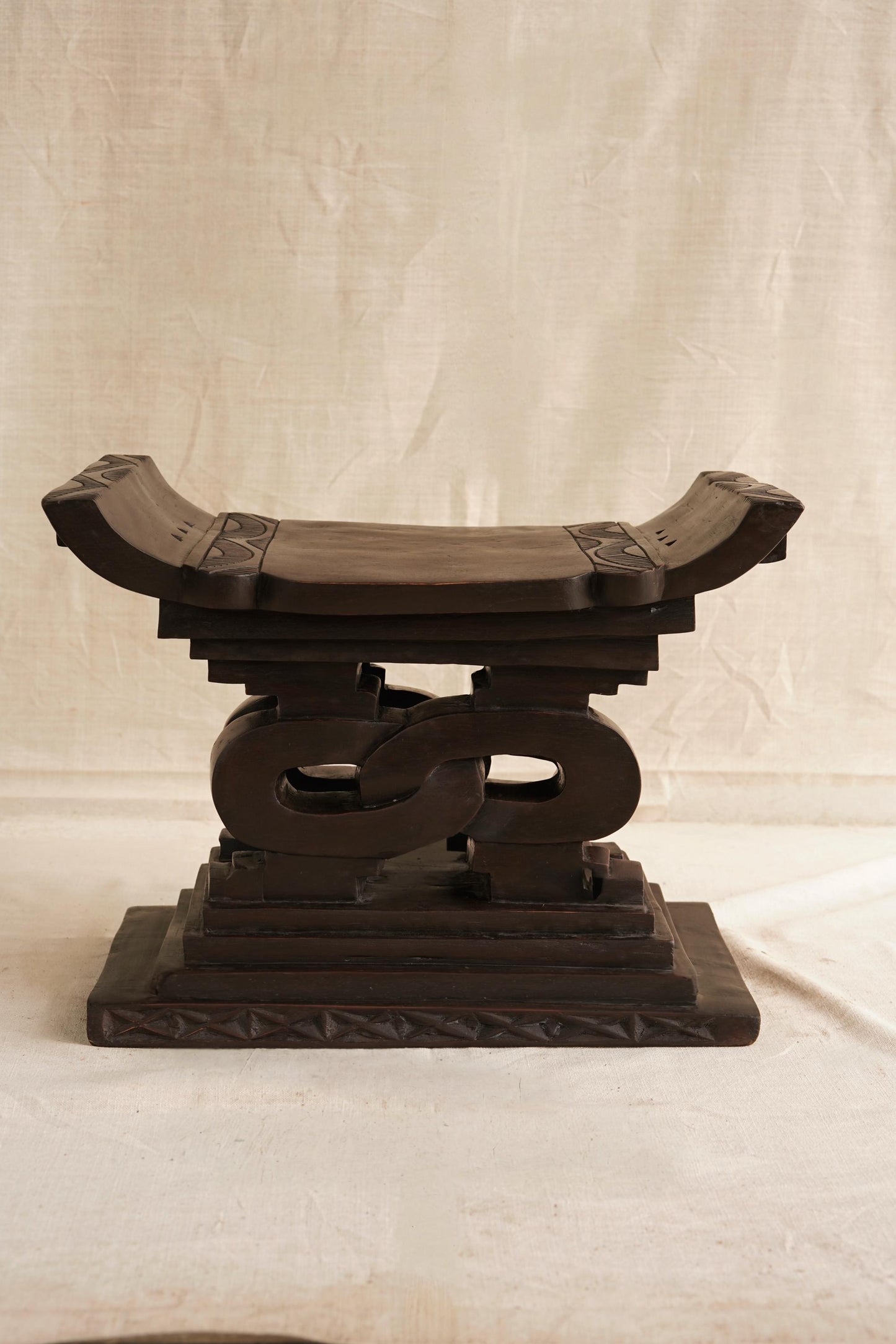 A hand-carved wooden Ashanti stool with a curved seat and arched base, featuring detailed motifs.