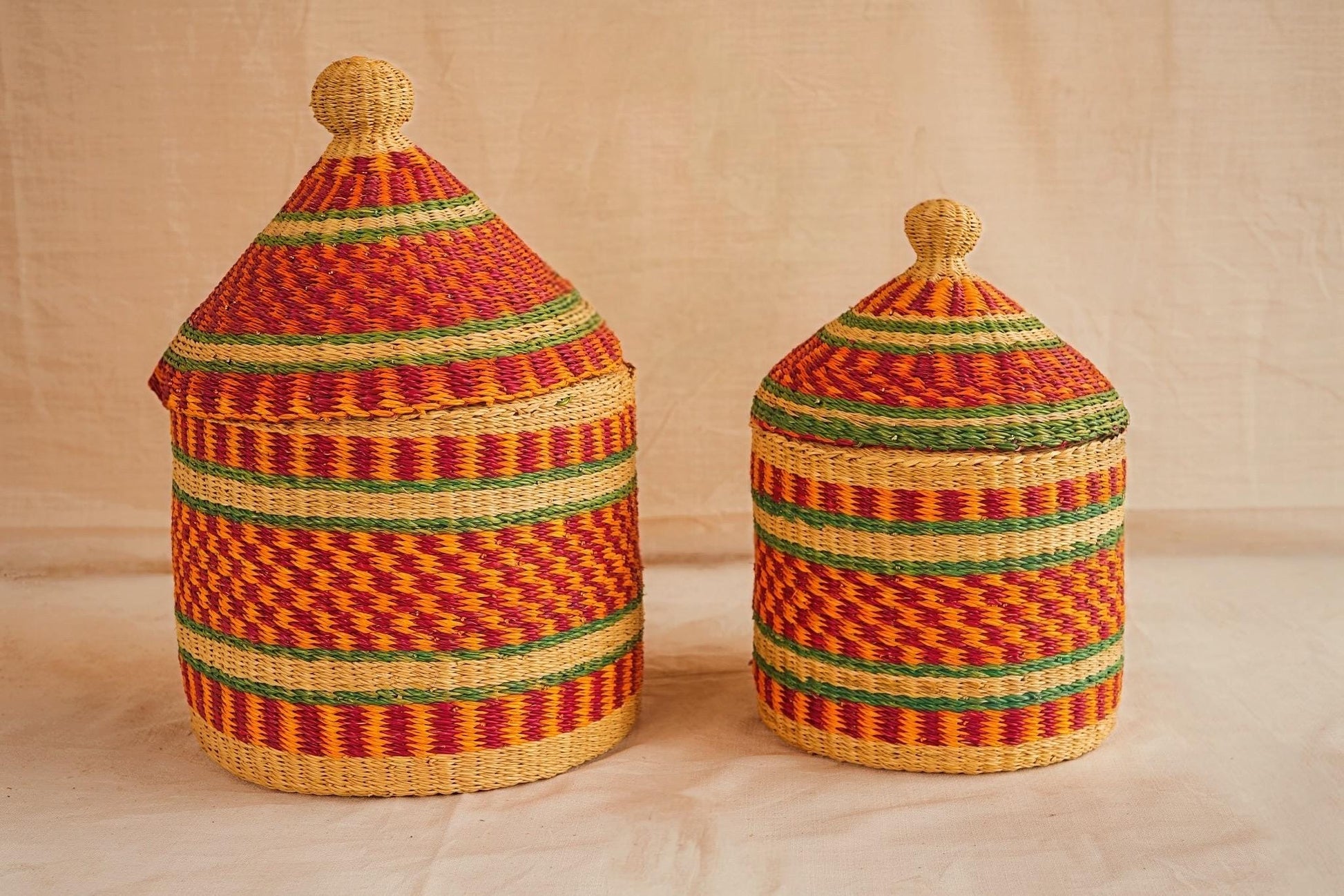 Two handwoven Bolga storage baskets in red, green, and beige patterns with leather-wrapped handles.