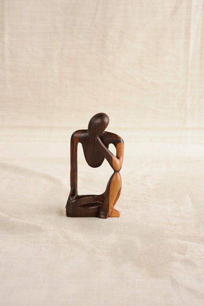 Wooden sculpture of a seated figure on a draped fabric background