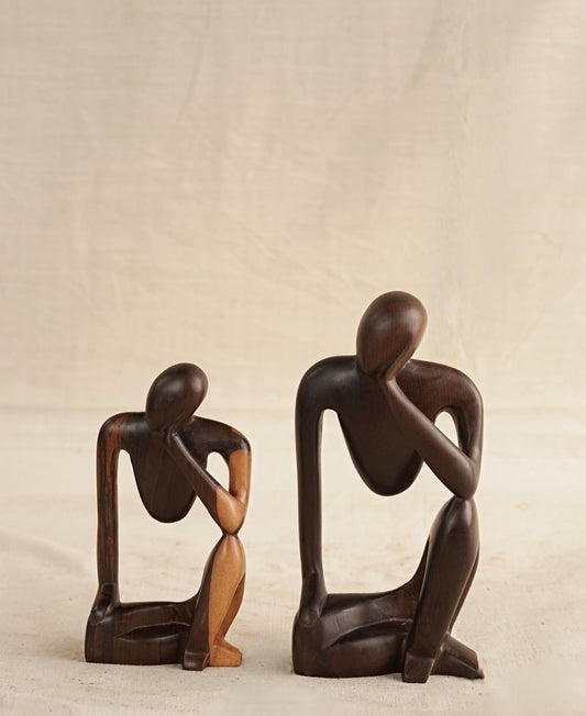 Two wooden figurines of a thinking man, one larger than the other, carved from ebony wood with a polished finish.