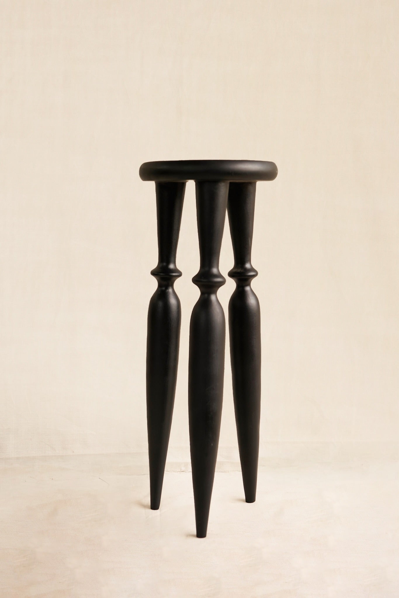 Black stool with thin legs on a beige background