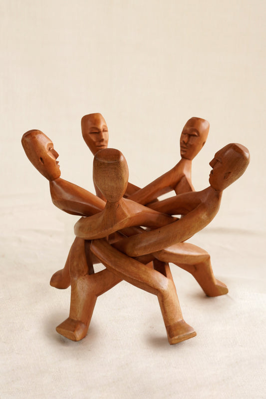 Wooden sculpture of five interlocking figures on a beige background