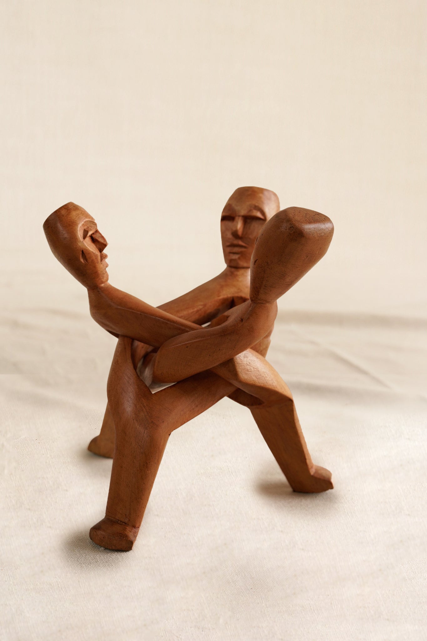 Wooden sculpture of two figures embracing on a beige background