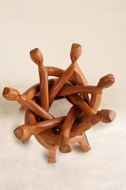Wooden sculpture of intertwined figures on a beige background